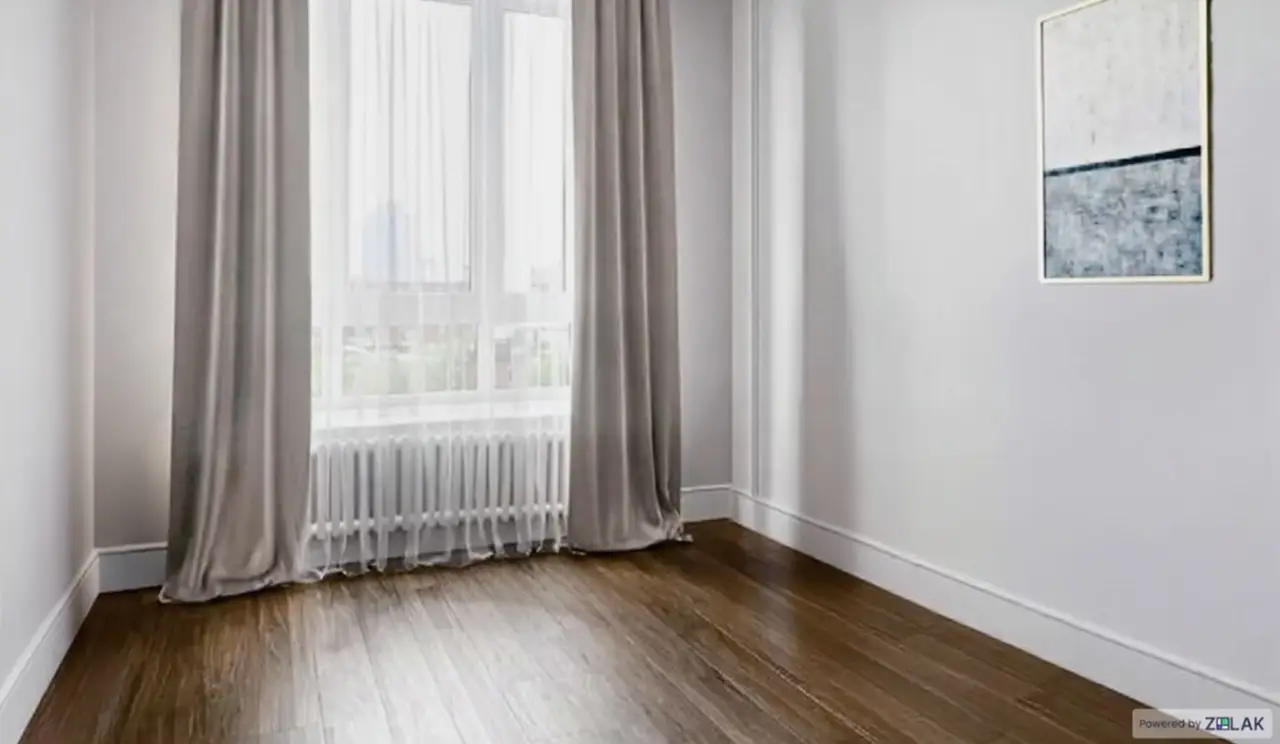 An empty room with bare floor and a radiator under the window
